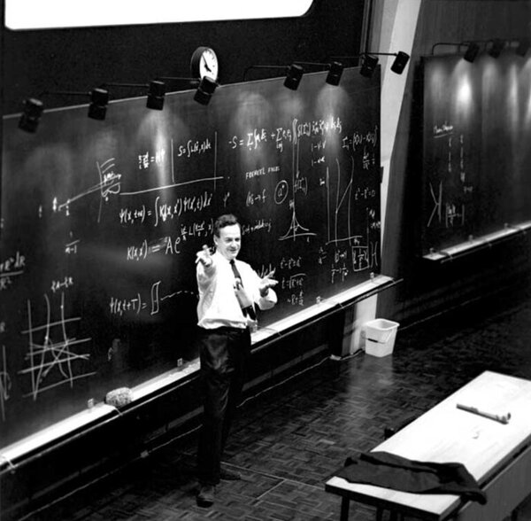 Richard Feynman lecturing in front of a blackboard covered with equations, diagrams and boxed results
